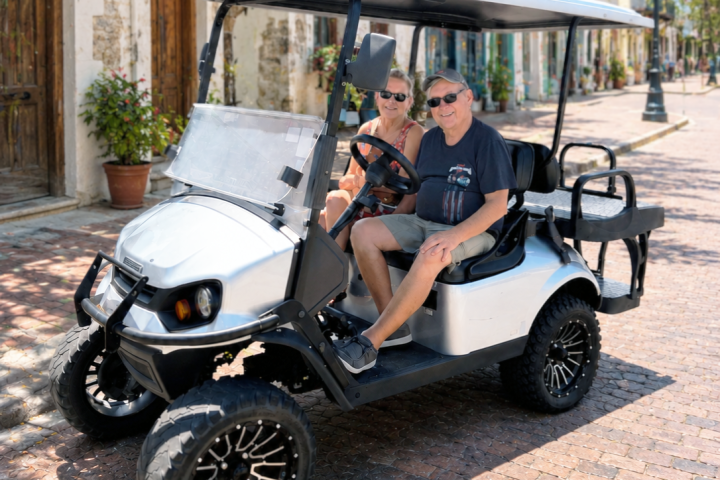 Two people sitting in a parked golf cart on a cobblestone street.