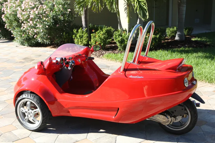 Red three-wheeled scooter with a sporty design parked on a paved area.