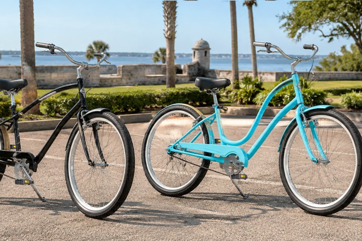 Two bicycles, one black and one blue, parked in a lot by the waterfront.