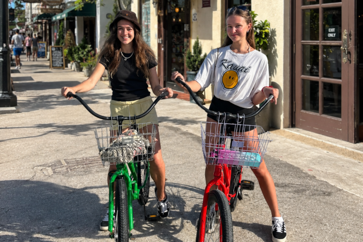 Two young women on colorful bicycles smiling outdoors.