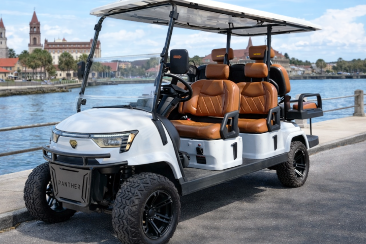 White luxury golf cart with brown seats parked by a waterfront.