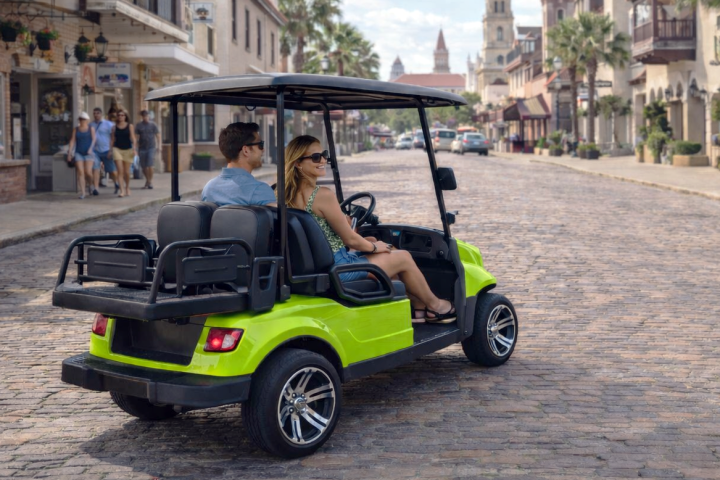 Couple in a bright green golf cart on a historic cobblestone street.