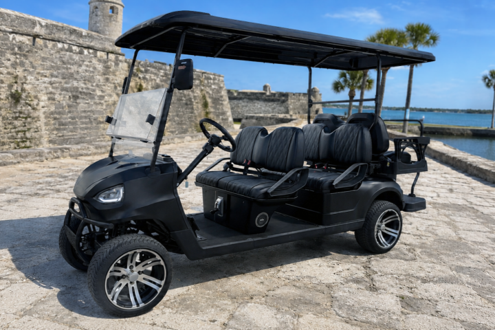 Black golf cart parked by a fort and water on a sunny day.