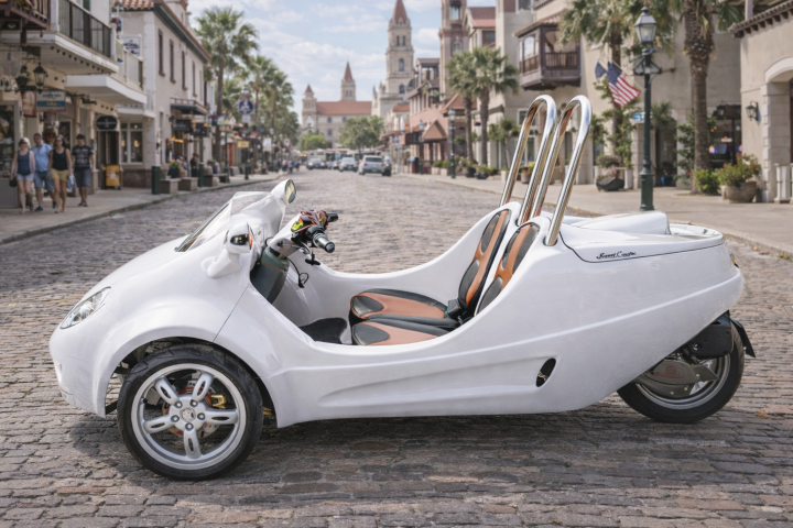 White three-wheeled vehicle parked on a cobblestone street in a scenic town.