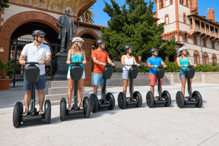 Six people on Segways wearing helmets in front of a historic building.