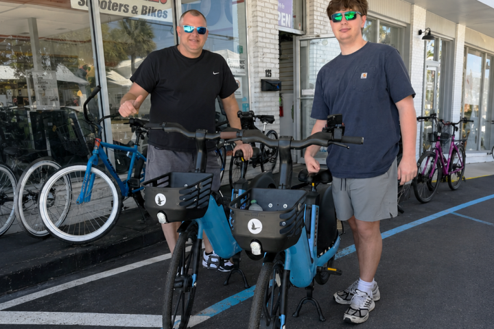 Two people standing with electric bikes outside a store.