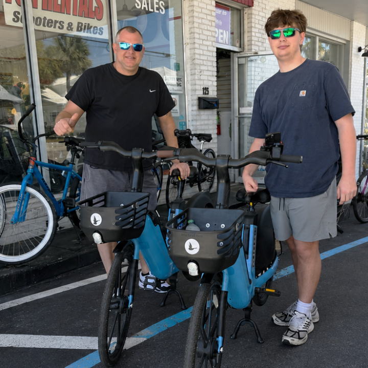 Two people with e-bikes outside a store on a sunny day.