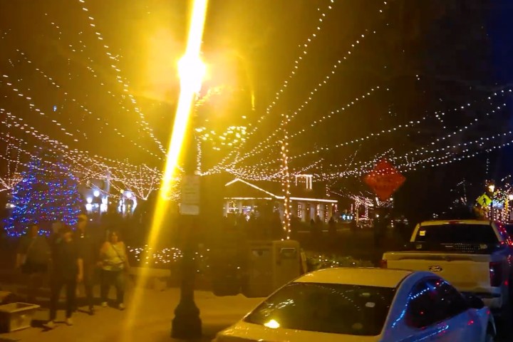 Street with festive lights, people, and parked cars at night.