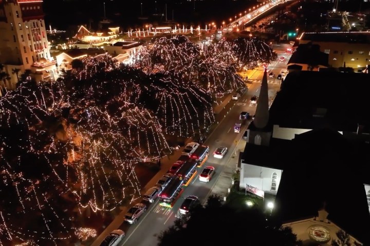Aerial view of a city street lit with festive holiday lights and traffic at night.