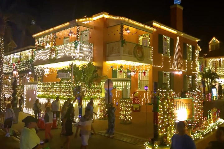 Festively lit house with holiday decorations at night, people walking by.