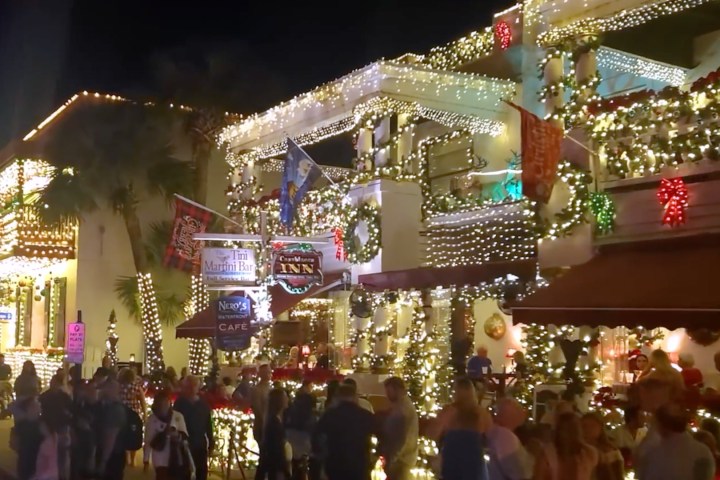 Festive street scene with colorful lights on decorated buildings and a crowd of people.