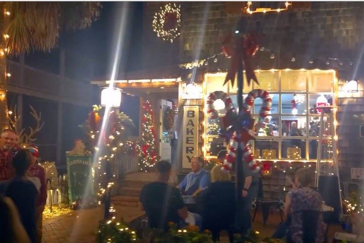 Festively decorated bakery with lights and candy canes, people gathered outside.