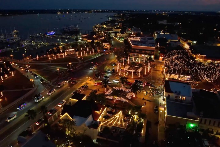 Aerial view of a coastal town at night, illuminated with festive lights.